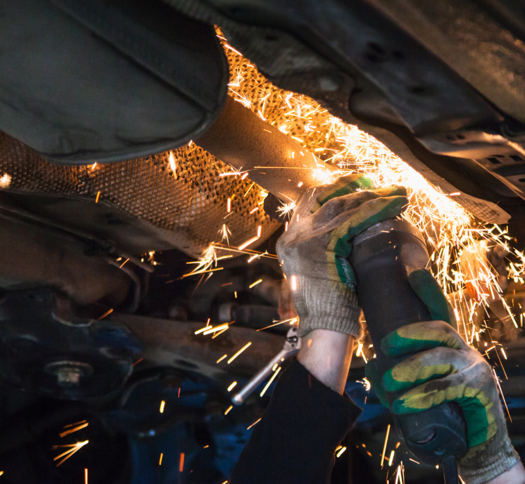 A welder is working on a car, creating sparks as they join metal parts, showcasing skilled craftsmanship.